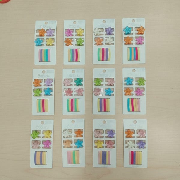 Doce tarjetas exhibidoras con mini broches de plástico en forma de flor y colitas elastizadas para el pelo en varios colores.