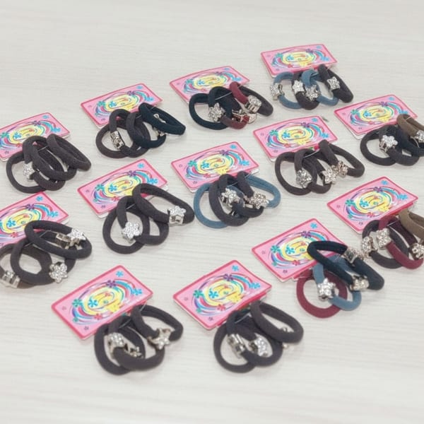 Doce tarjetas exhibidoras con colitas para el pelo elásticas en colores surtidos y dijes brillantes.