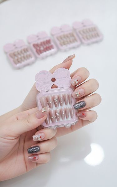 Cajas de uñas postizas decoradas en tonos rosa, nude y negro con brillos y apliques