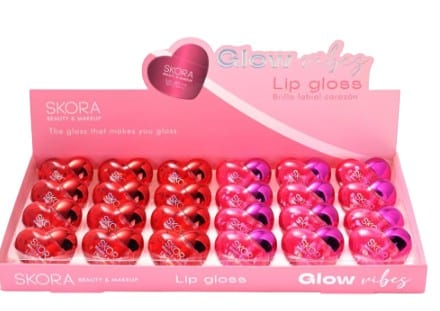 Caja exhibidora rosa con 24 brillos labiales Skora en forma de corazón rojos y fucsias.