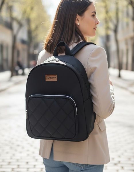 Mochila urbana negra con bolsillo frontal con diseño matelassé y parche decorativo superior.
