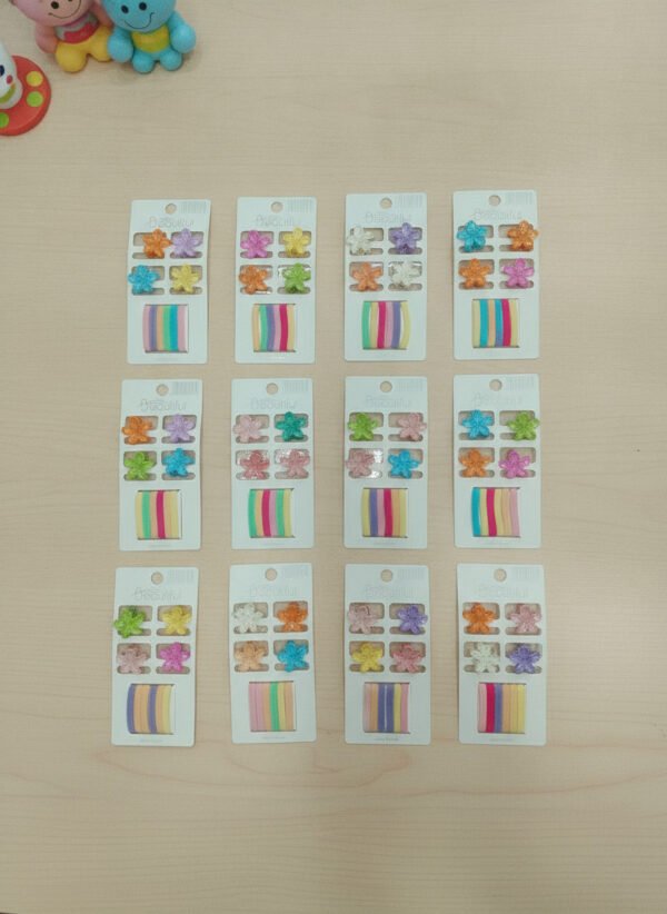 modacool-broches-y-colitas-flores-comercial-1.jpg Doce tarjetas exhibidoras con mini broches de plástico en forma de flor y colitas elastizadas para el pelo en varios colores.